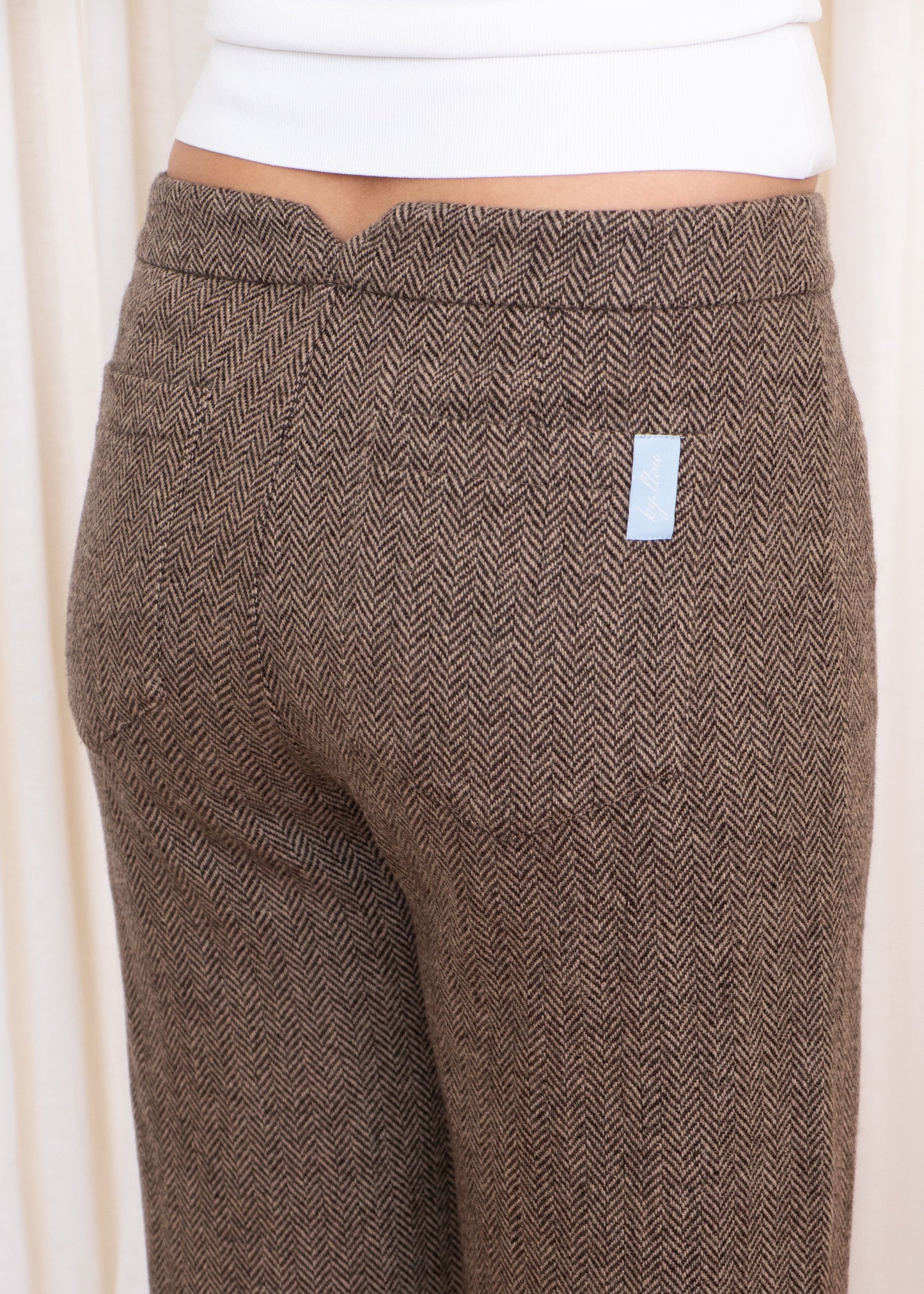 Brown herringbone patterned pants with a small white label on a light background