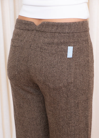 Brown herringbone patterned pants with a small white label on a light background