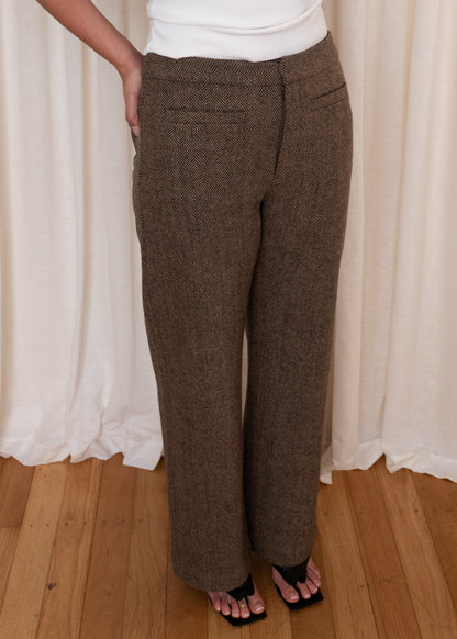 Person wearing brown pants and a white top against a white curtain background